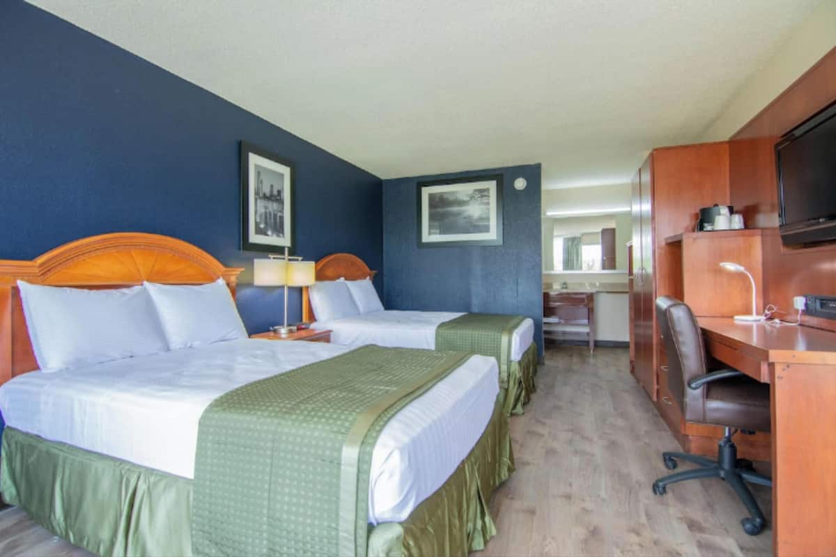 A hotel room with two beds, a desk, a chair, a TV, and a mirror.