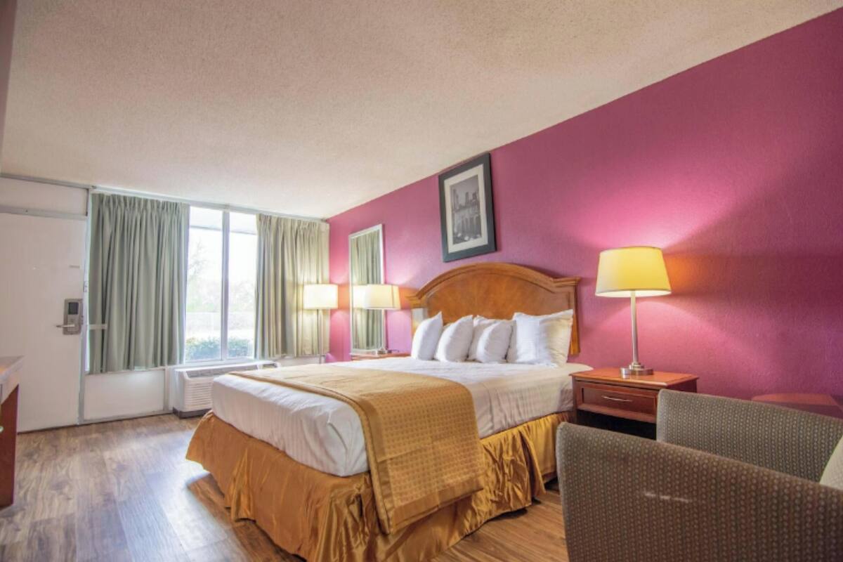 A hotel room with a bed, two bedside tables, a chair, a window with curtains, and a picture on the wall.