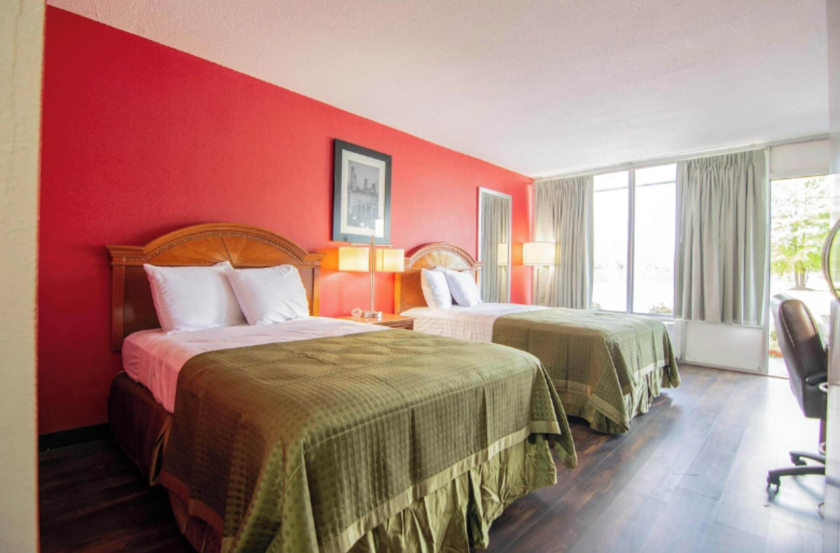 A hotel room with two beds, red walls, and a large window with curtains.