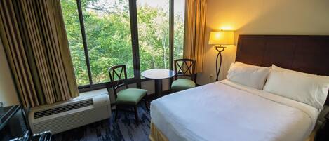 Une chambre d’hôtel avec un lit, une table, deux chaises, une lampe et une fenêtre avec des rideaux.