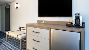 Une chambre d’hôtel moderne équipée d’un téléviseur à écran plat fixé au mur, d’un minibar, d’un petit coin salon et d’une machine à café.