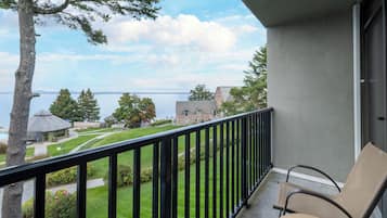 A balcony with a chair, overlooking a landscaped area with a building and a body of water in the distance.