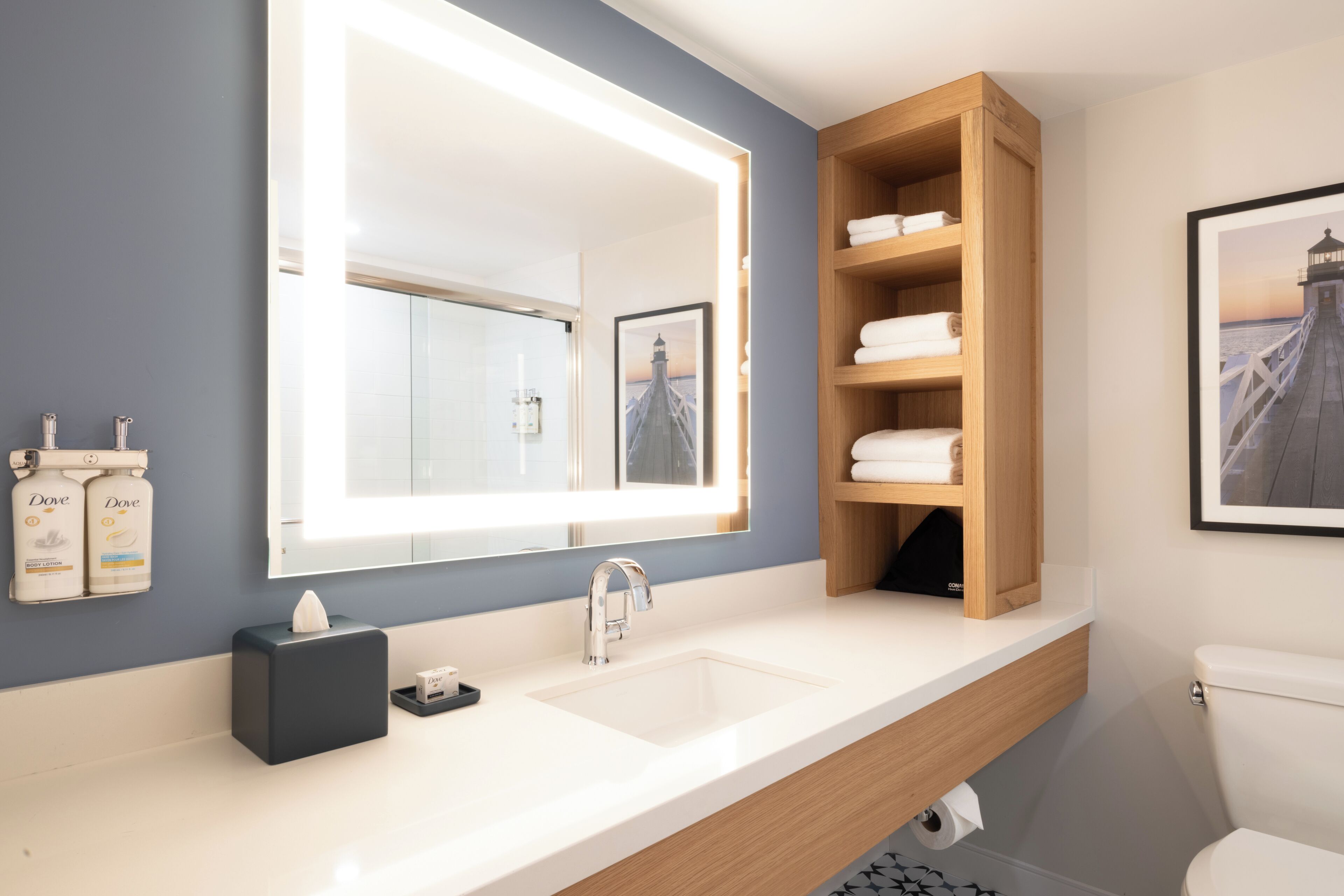 Een moderne badkamer met een grote spiegel, een witte wastafel, een houten opbergmeubel en een toilet.