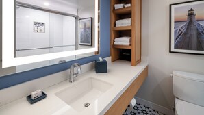 Ein modernes Badezimmer mit einem großen Spiegel, einem weißen Waschbecken, einem Holzregal mit Handtüchern und einem Bild von einem Steg.