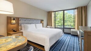 Ein Hotelzimmer mit Bett, rundem Tisch, Stuhl, Schreibtisch und einem Fenster mit Vorhängen.