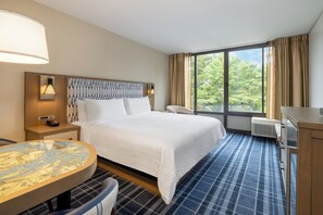 Ein Hotelzimmer mit Bett, rundem Tisch, Stuhl, Schreibtisch und einem Fenster mit Vorhängen.