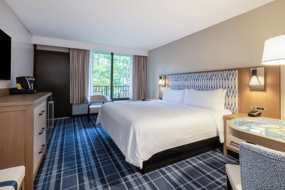 Een hotelkamer met een bed, bureau, stoel, televisie en een balkon met gordijnen.