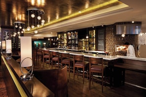 Zona de bar con varios taburetes, una barra y una variedad de botellas y vasos.
