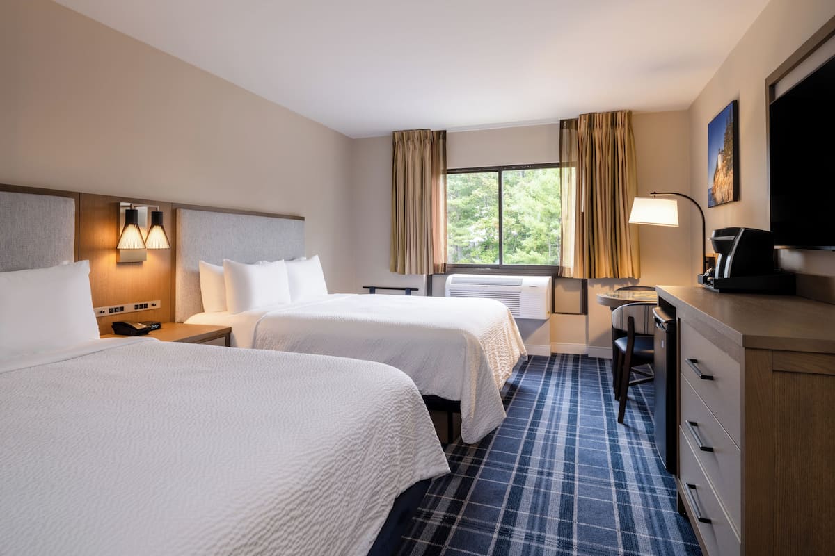 Ein Hotelzimmer mit zwei Betten, einem Schreibtisch, einem Stuhl, einem Fernseher und einem Fenster mit Vorhängen.