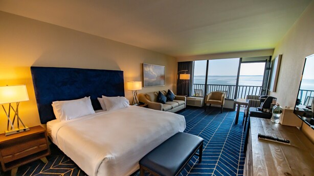 Une chambre d’hôtel avec un grand lit, un canapé, un bureau et une vue sur l’océan.