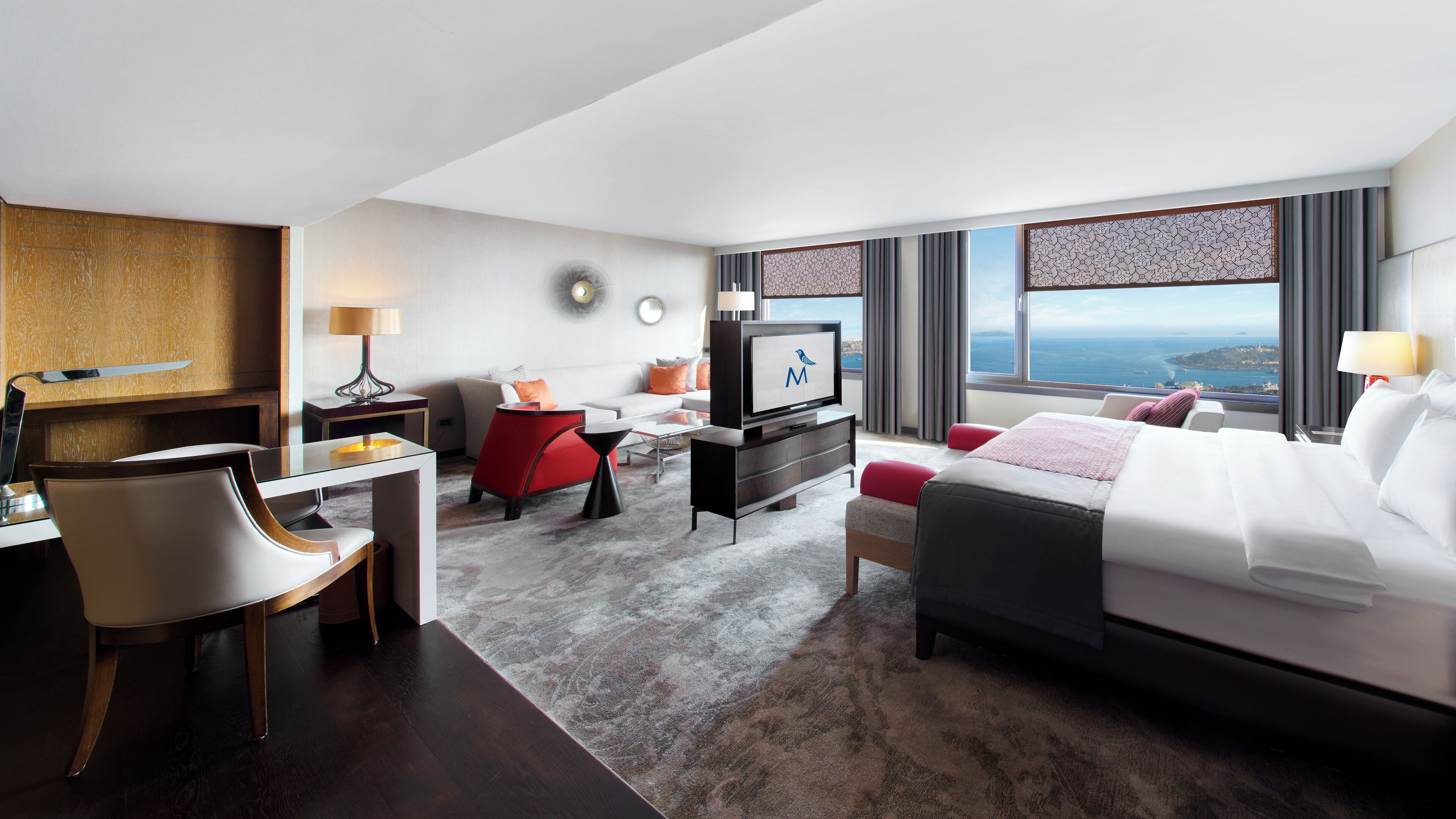 Habitación de hotel con cama, escritorio con silla, televisor y vista al mar.