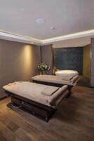 Un cuarto de spa con dos camillas de masaje, una bañera grande y un espejo que refleja la habitación.