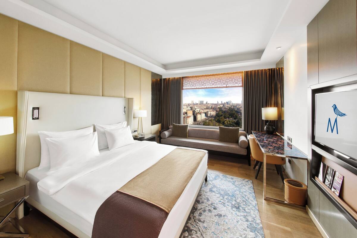 A hotel room with a large bed, a desk, a sofa, and a view of the city.
