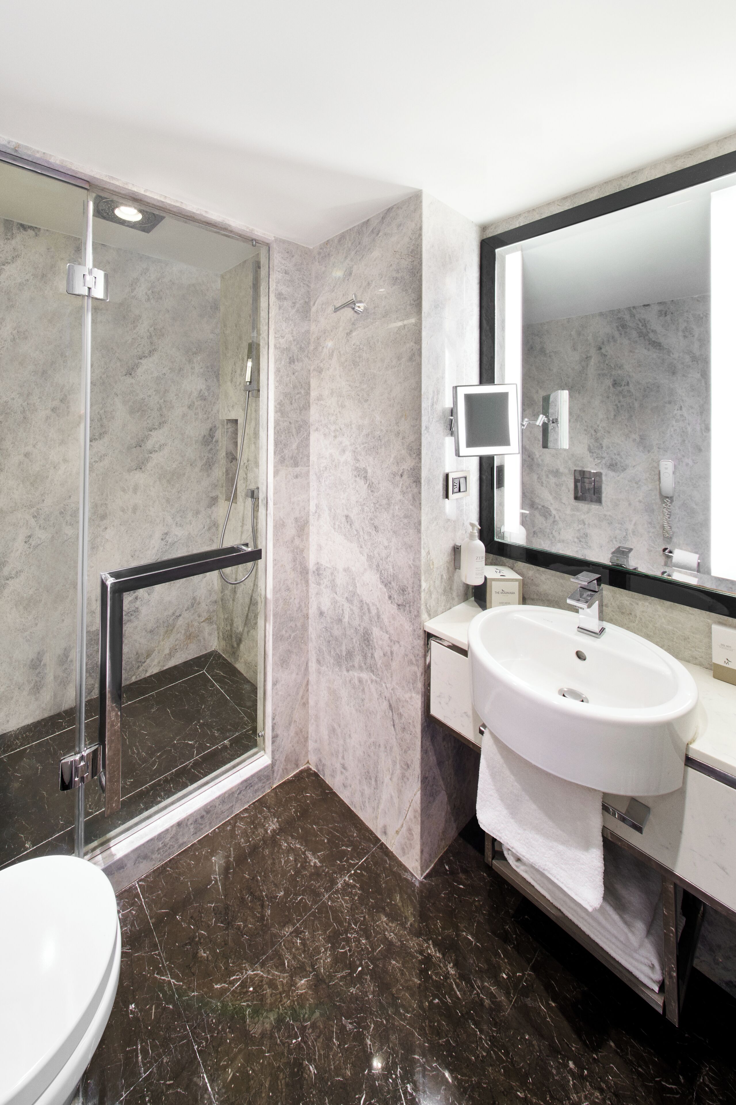 Een moderne badkamer met een douche met glazen wand, een witte wastafel en een grote spiegel.