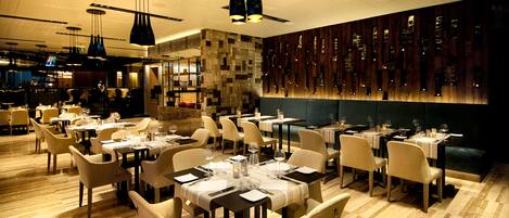 Un restaurante con varias mesas y sillas, una pared de piedra y lámparas colgantes.