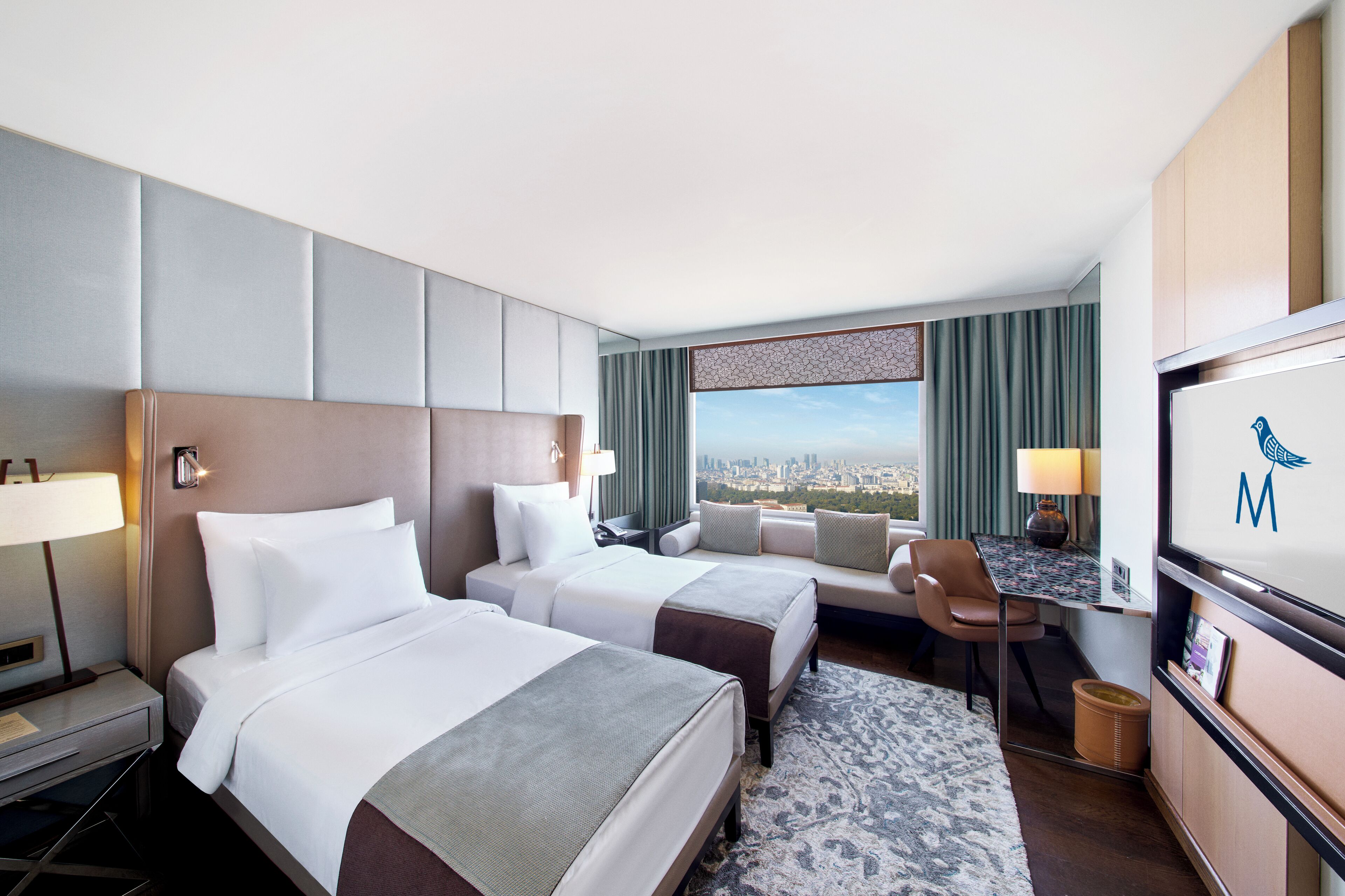 A hotel room with two beds, a desk, a chair, a TV, and a view of the city.