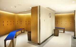 Een hotel lobby met houten kluisjes, een blauwe bank, afvalbakken en een klok aan de muur.
