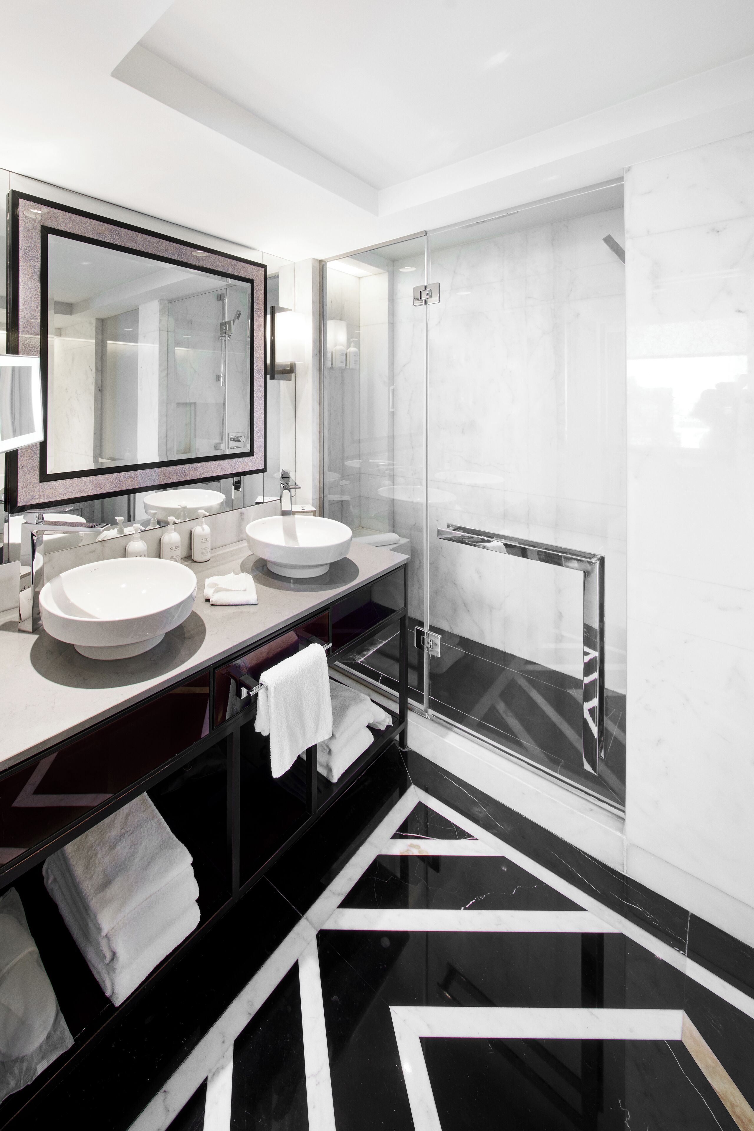 A modern bathroom with two sinks, a large mirror, and a glass shower enclosure.