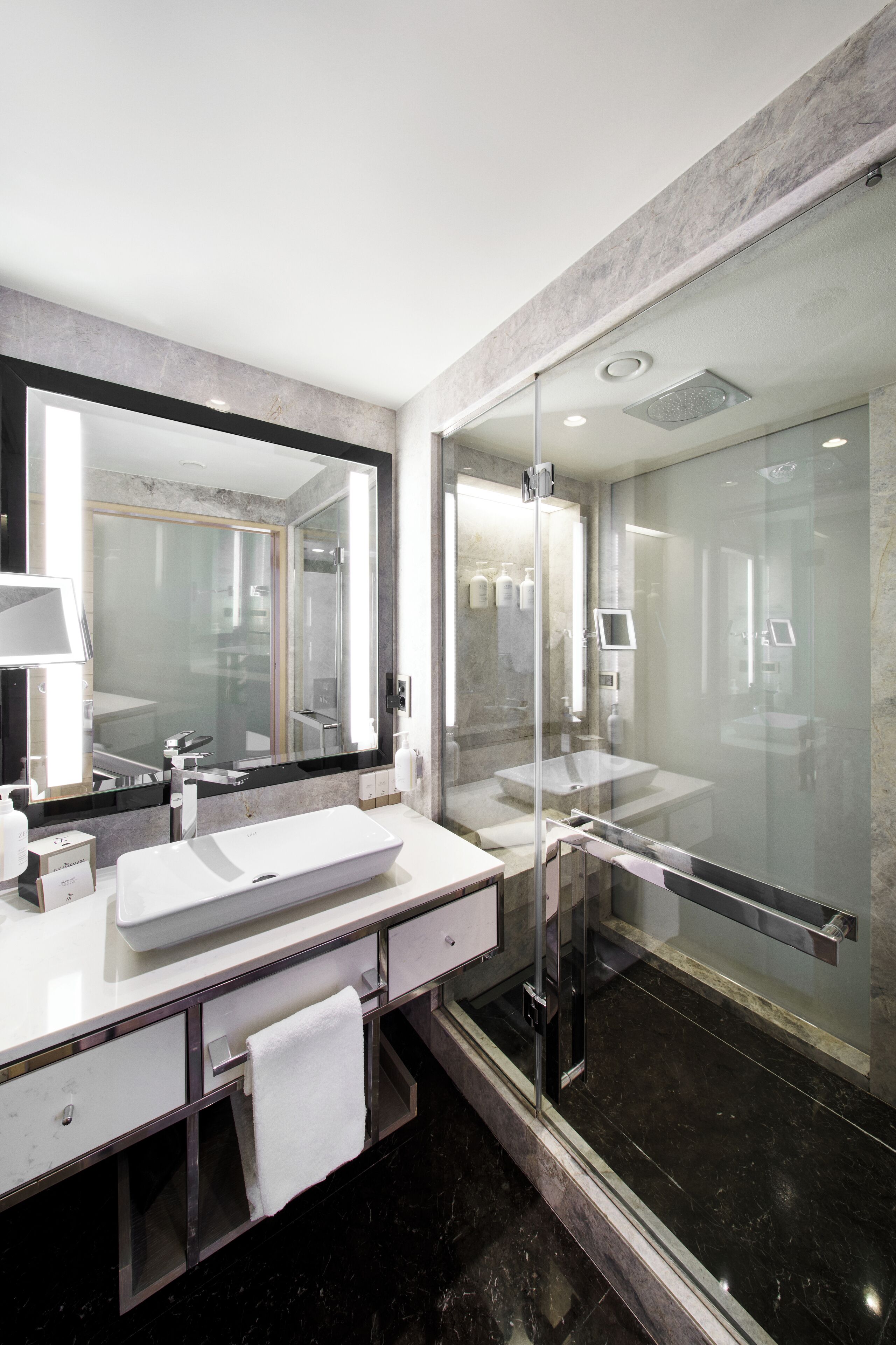 A modern bathroom with a large mirror, a glass-enclosed shower, and a white sink.