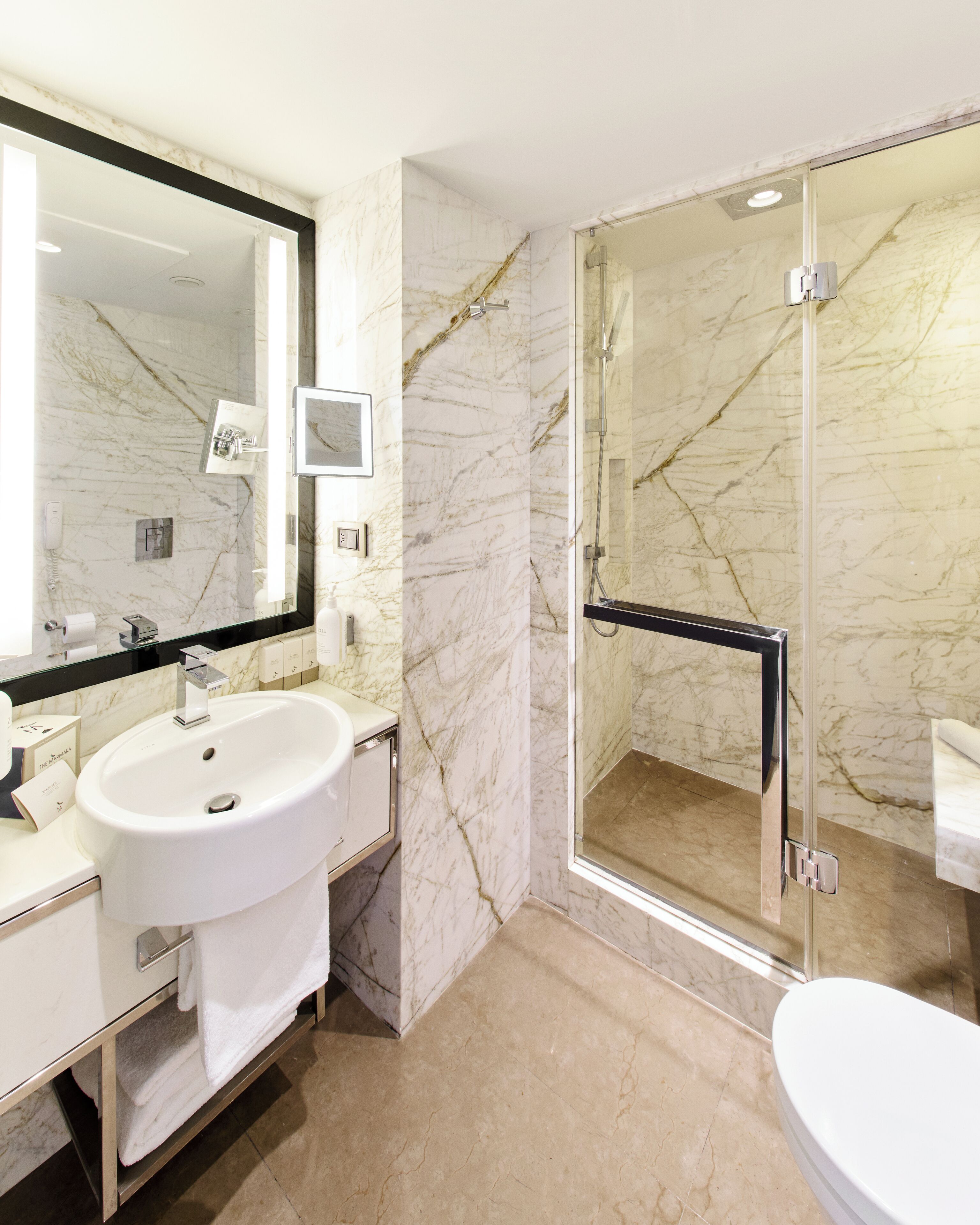 Une salle de bain moderne avec un lavabo en marbre, un grand miroir et une douche à parois de verre.