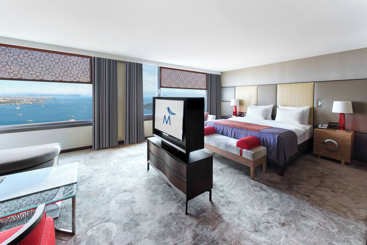 A hotel room with a bed, a TV, a desk, and a view of the city.