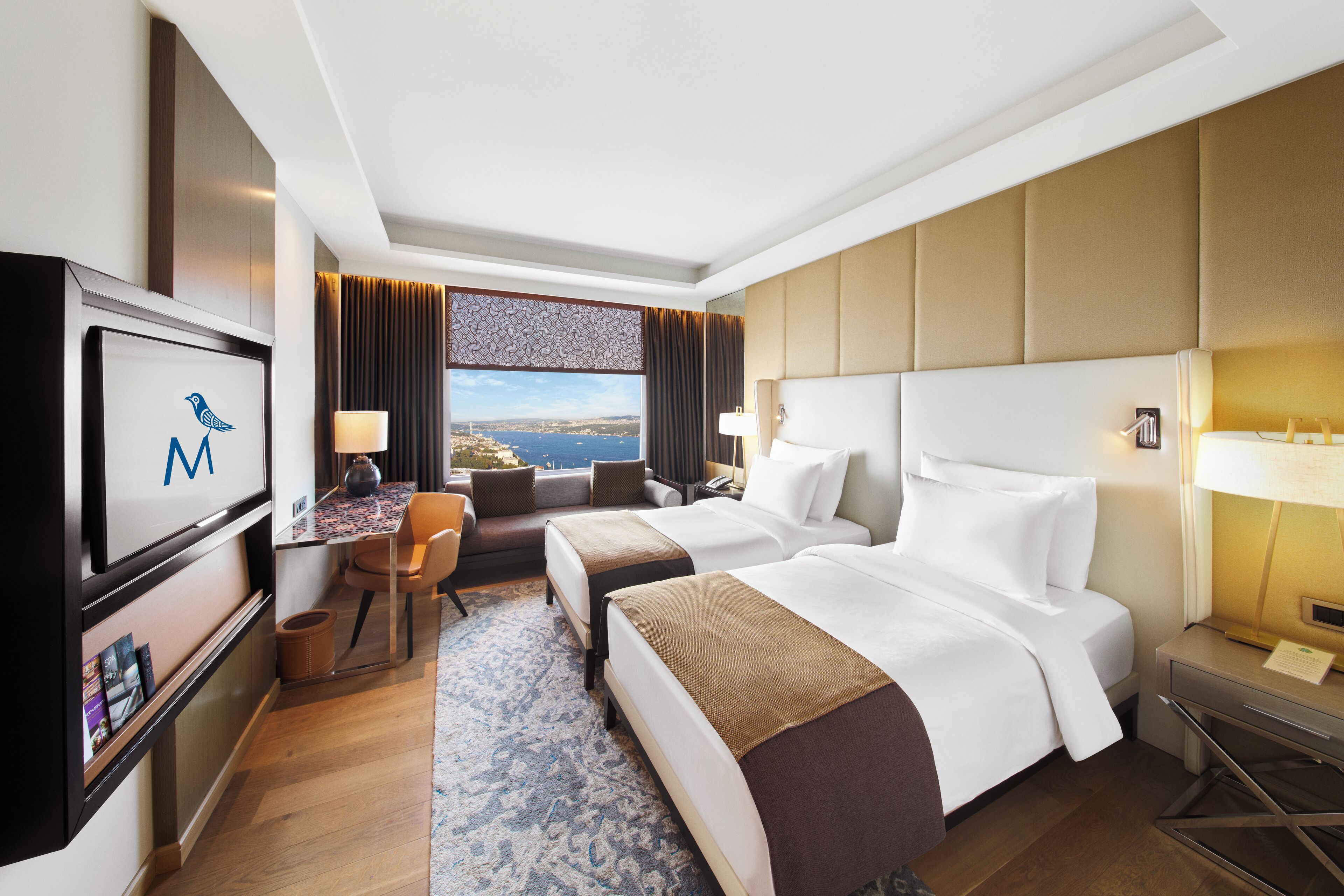 A hotel room with two beds, a desk, a chair, a TV, and a view of the city.