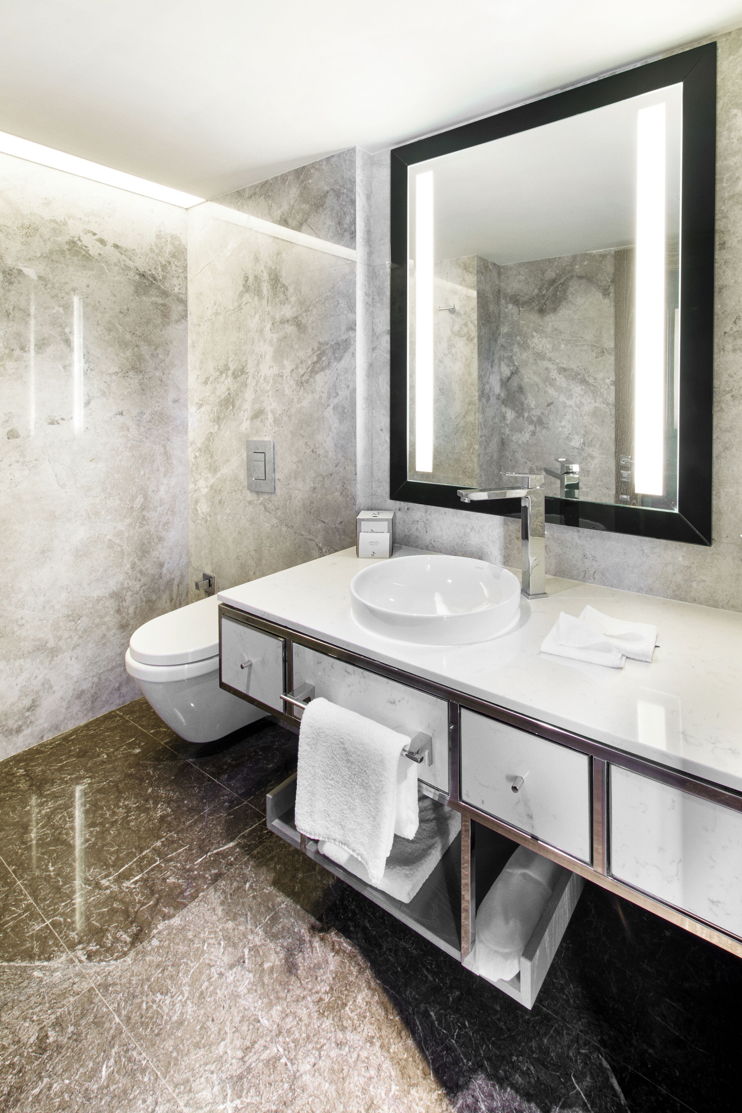 Un baño moderno con un lavamanos blanco, un espejo grande y paredes de mármol.