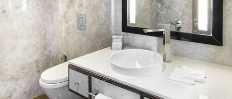 Un baño moderno con un lavamanos blanco, un espejo grande y paredes de mármol.