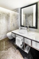 A modern bathroom with a white sink, a large mirror, and marble walls.
