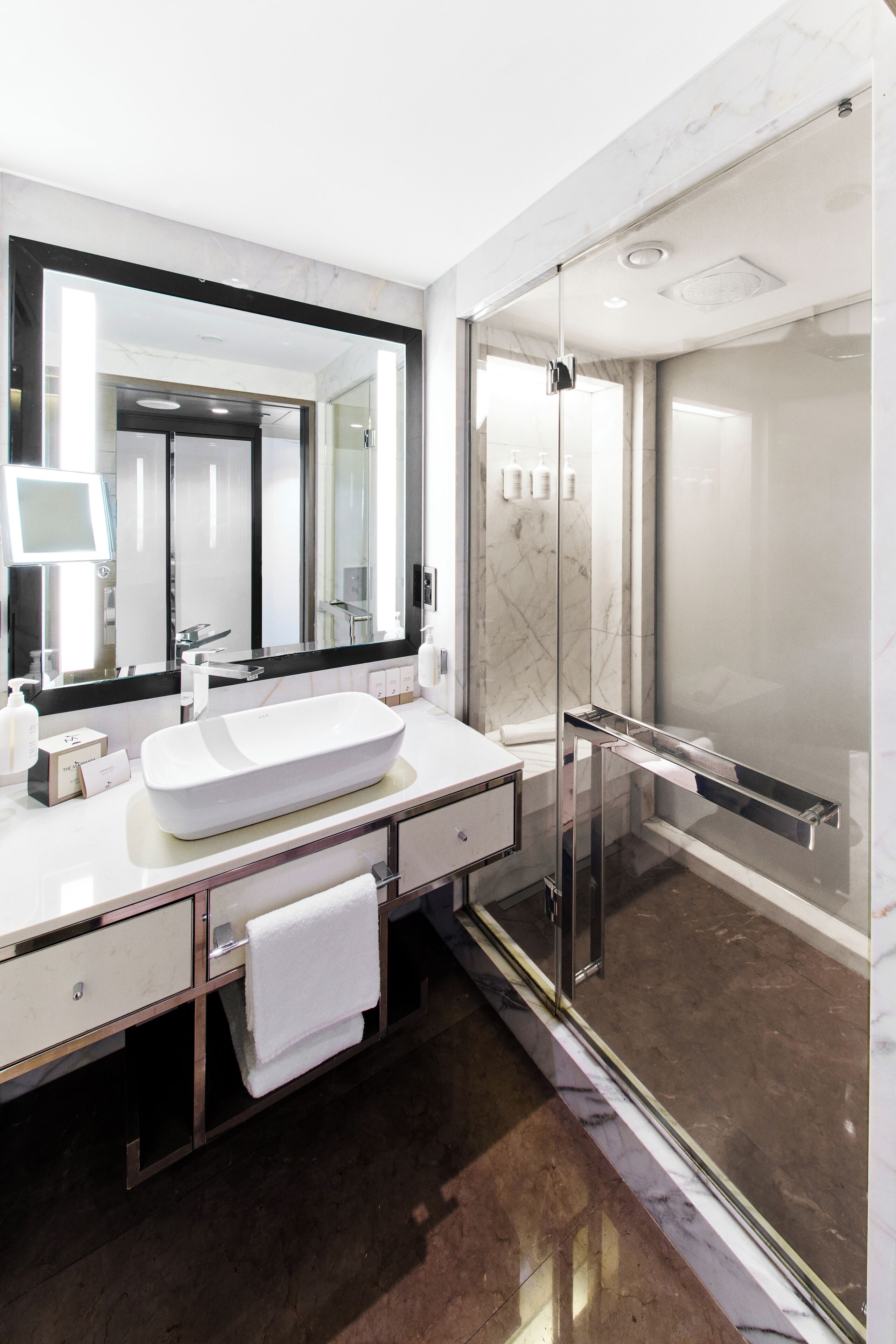 A modern bathroom with a large mirror, white sink, and glass shower enclosure.