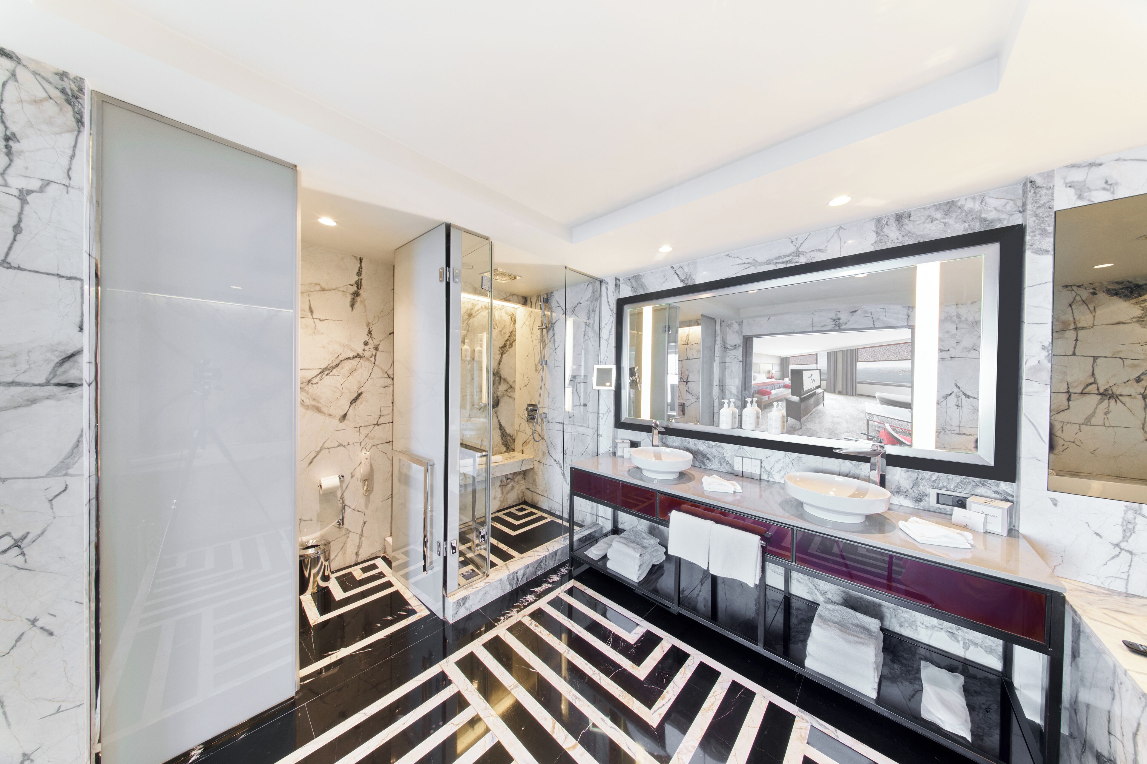 A modern bathroom with a large mirror, marble walls, and a black and white patterned floor.