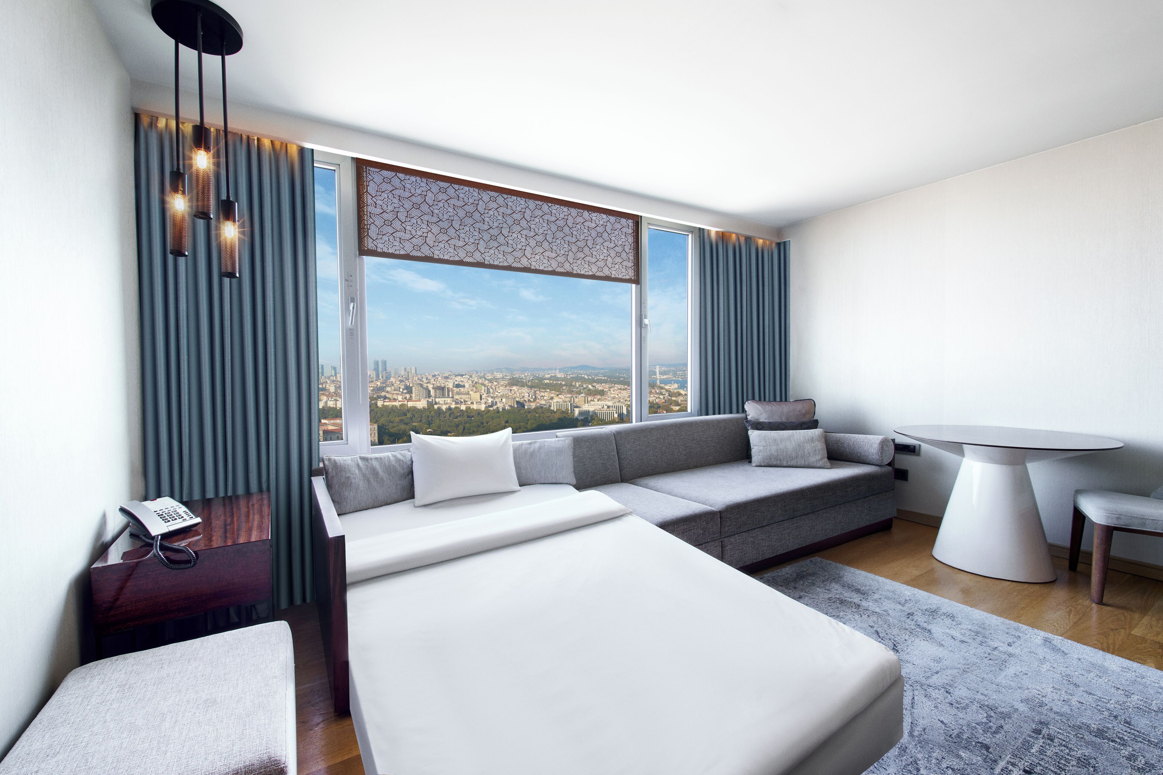 Una habitación de hotel moderna con una cama grande, un sofá, una mesa de comedor y vistas a la ciudad.