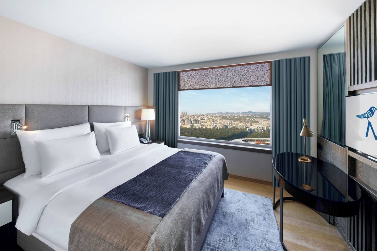 A hotel room with a large bed, a desk, and a view of a cityscape.