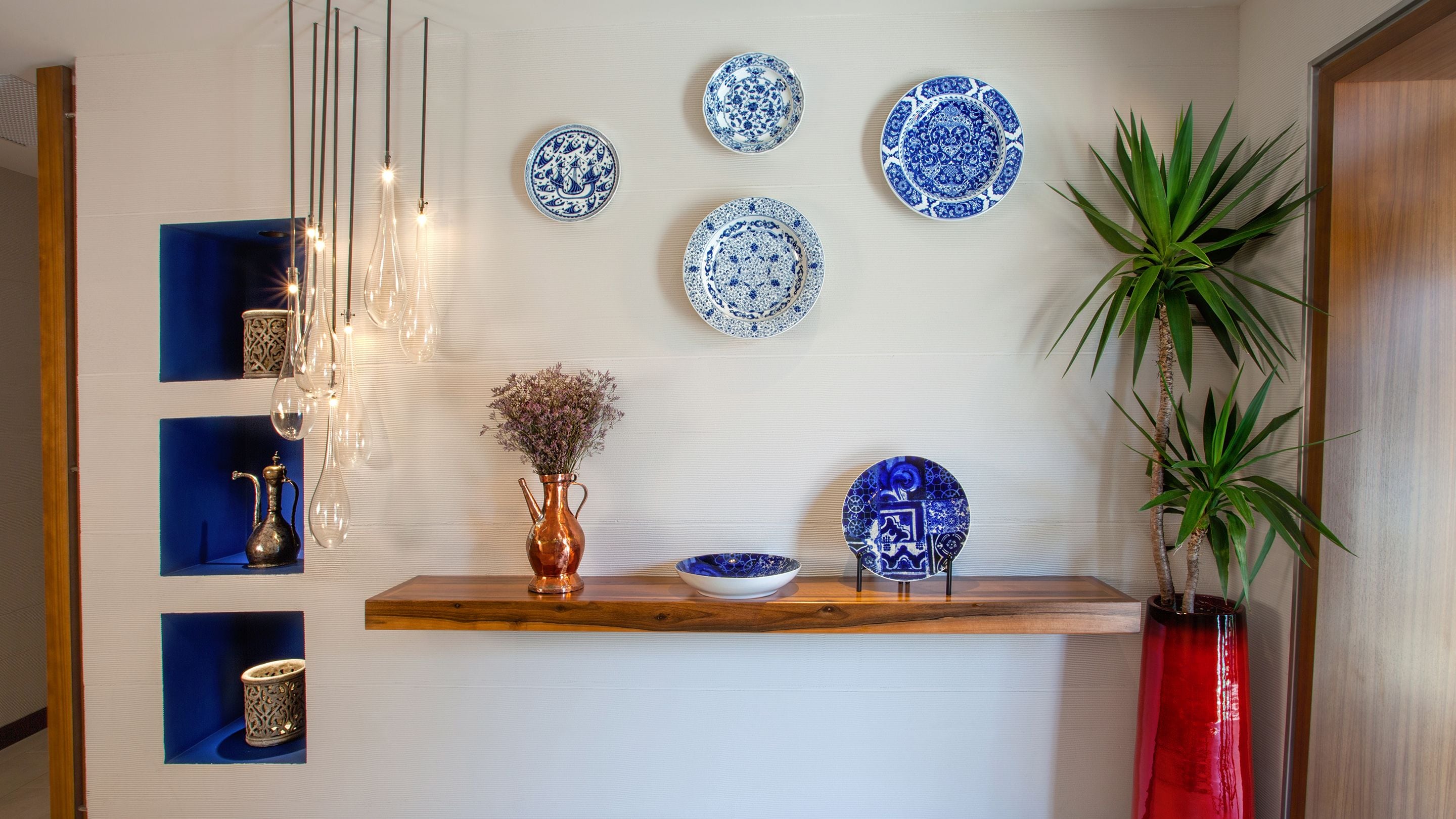 Una parete decorata con piatti ornamentali, un vaso con fiori secchi e una pianta.