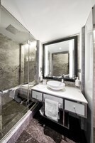 Un baño moderno con ducha envuelta en vidrio, un lavamanos blanco y un espejo grande.