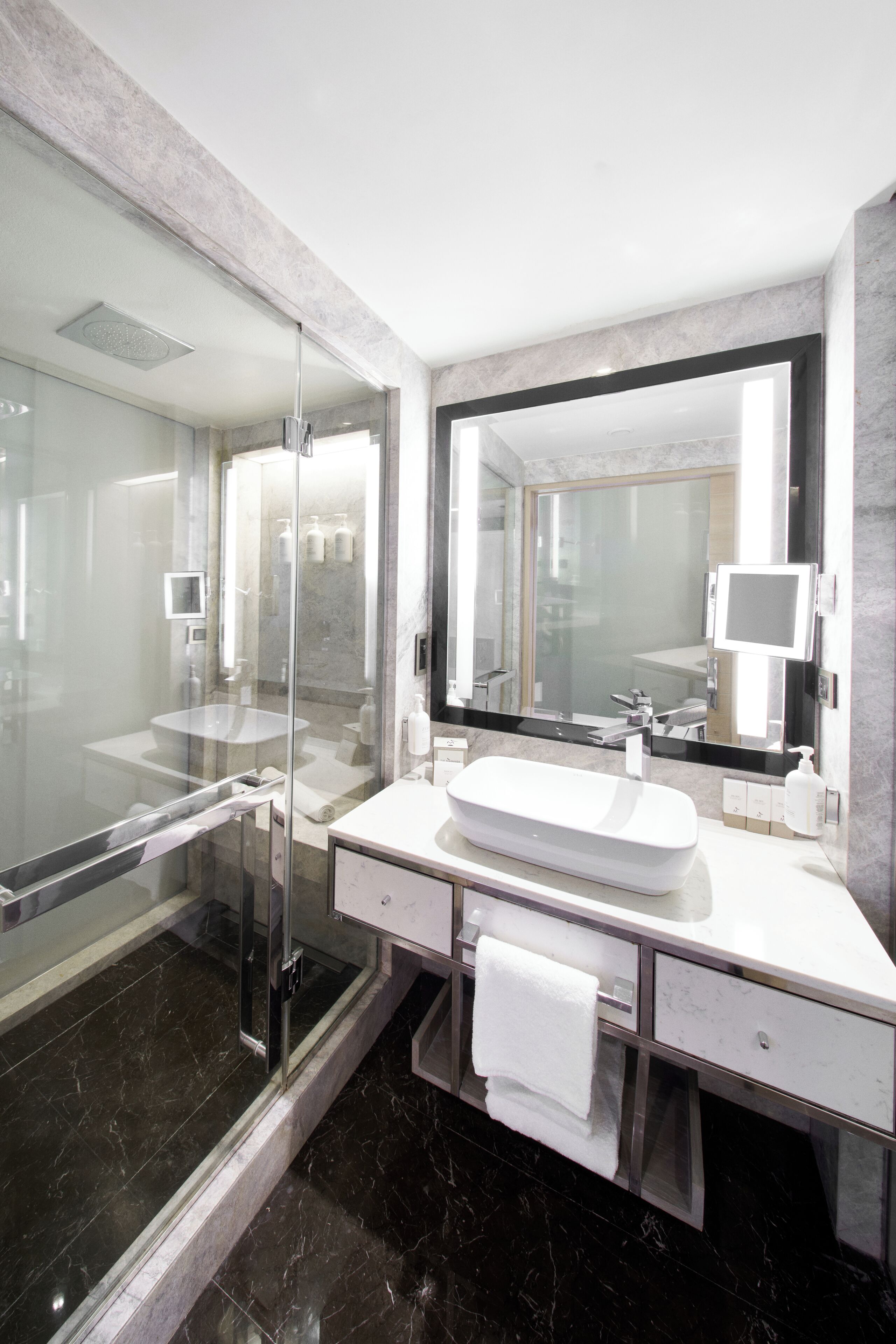 A modern bathroom with a glass-enclosed shower, a white sink, and a large mirror.