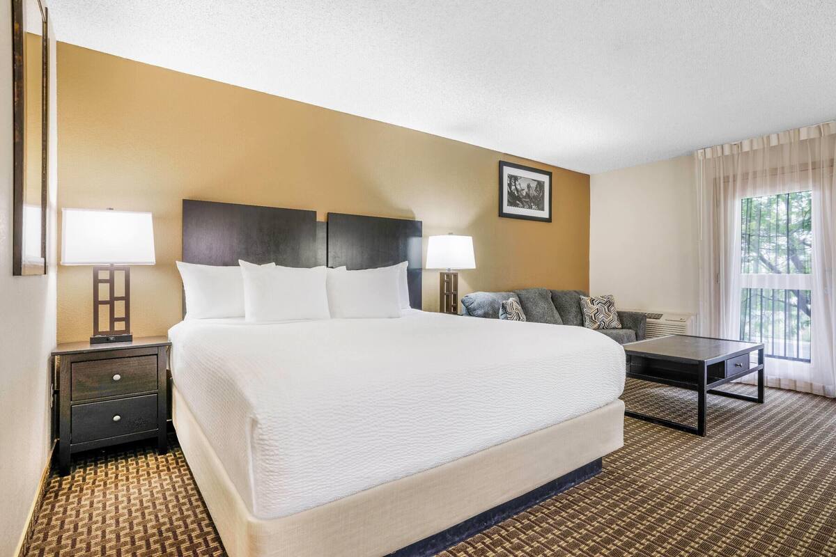 A hotel room with a large bed, two bedside tables with lamps, a sofa, and a window with curtains.