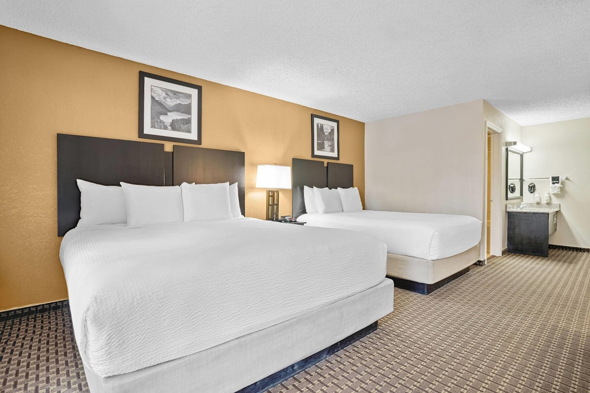 A hotel room with two beds, a nightstand, a lamp, and a bathroom visible through an open door.