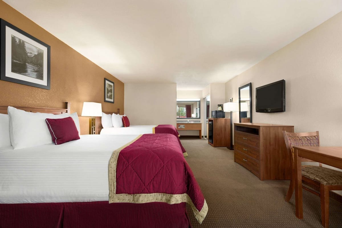 A hotel room with two beds, a desk, a dresser, a TV, and a mirror.