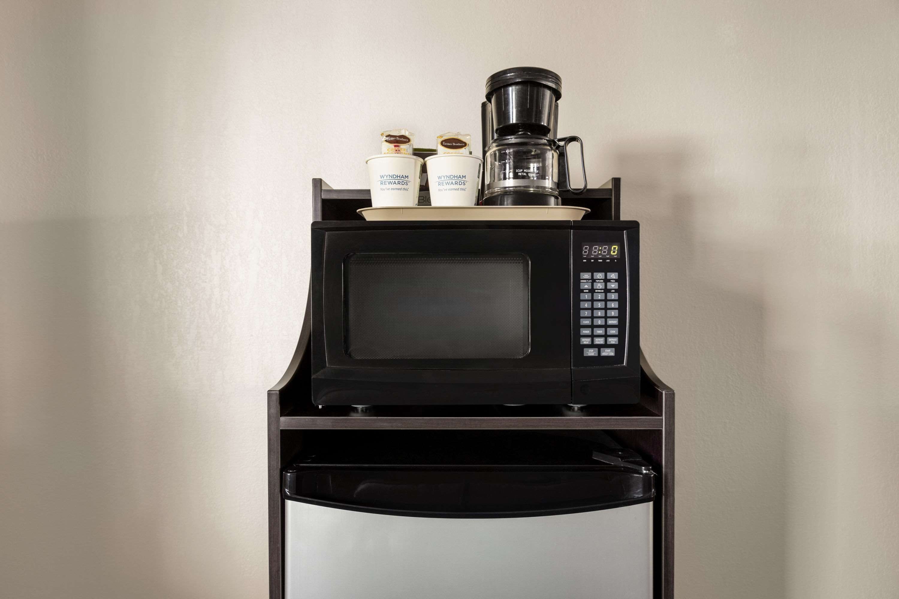 A black microwave with a coffee maker and two condiment bottles on top.
