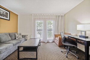 Habitación de hotel con sofá, escritorio, silla, mesita de centro y alfombra estampada.