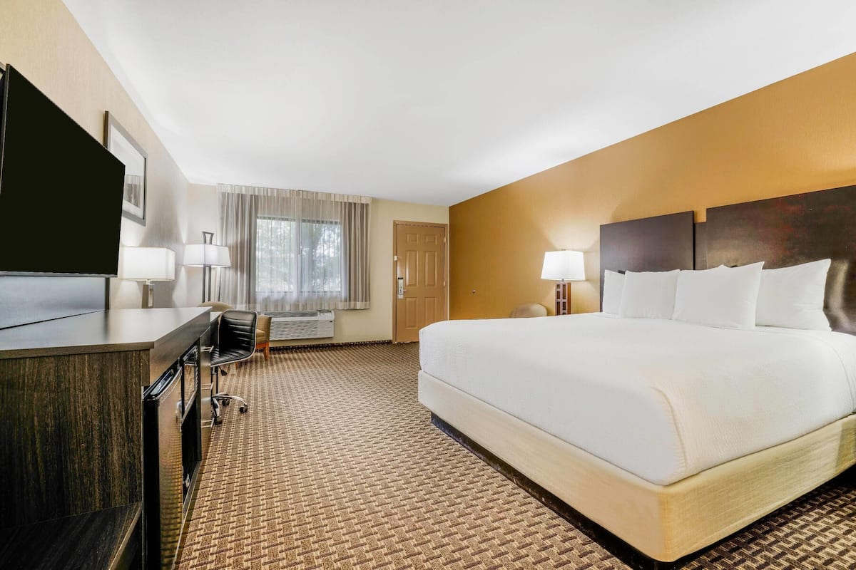 A hotel room with a large bed, a desk with a chair, a television, and a window with curtains.