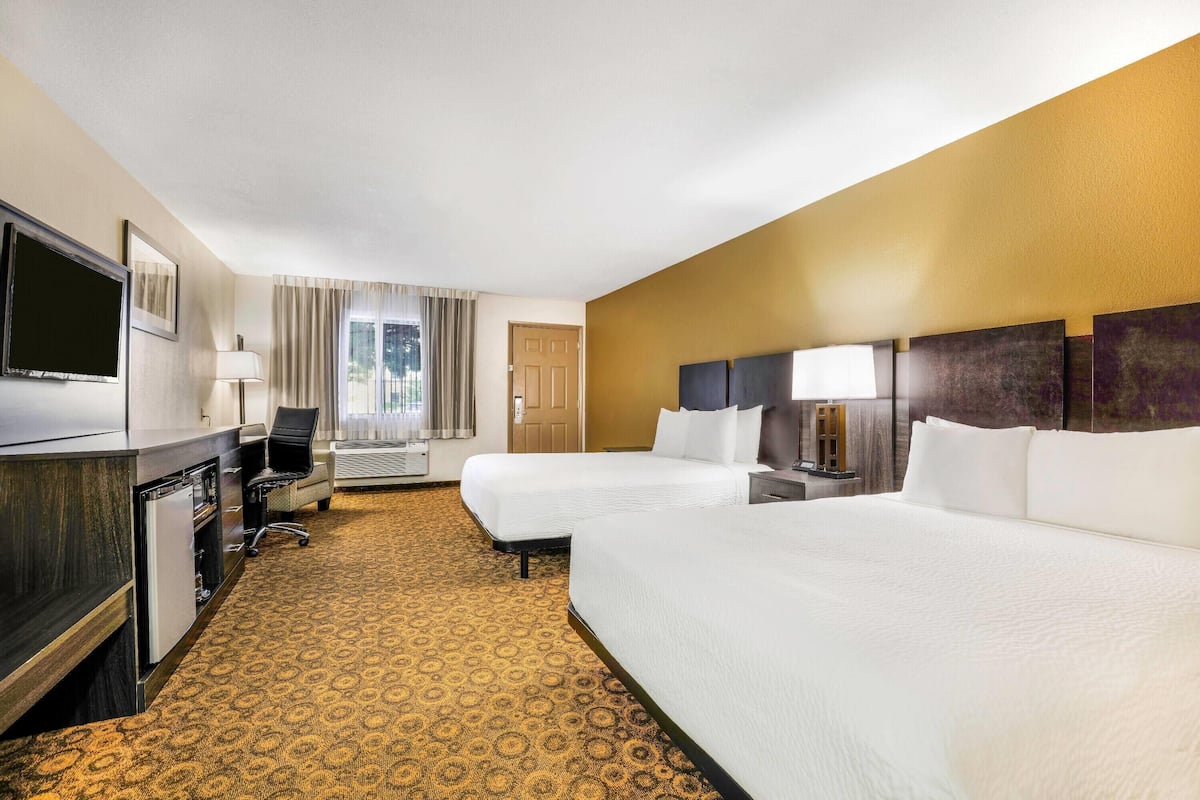 A hotel room with two beds, a desk, a TV, and a window with curtains.