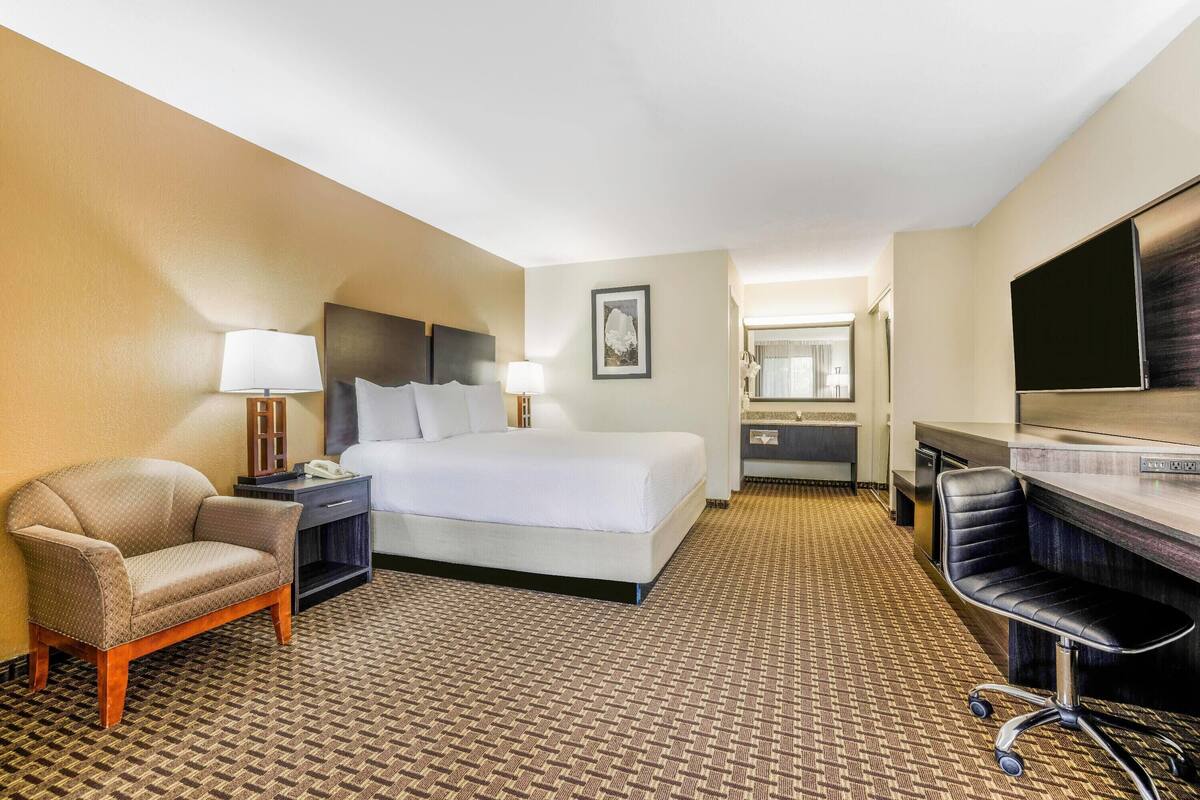 A hotel room with a bed, a chair, a desk, a TV, and a bathroom.