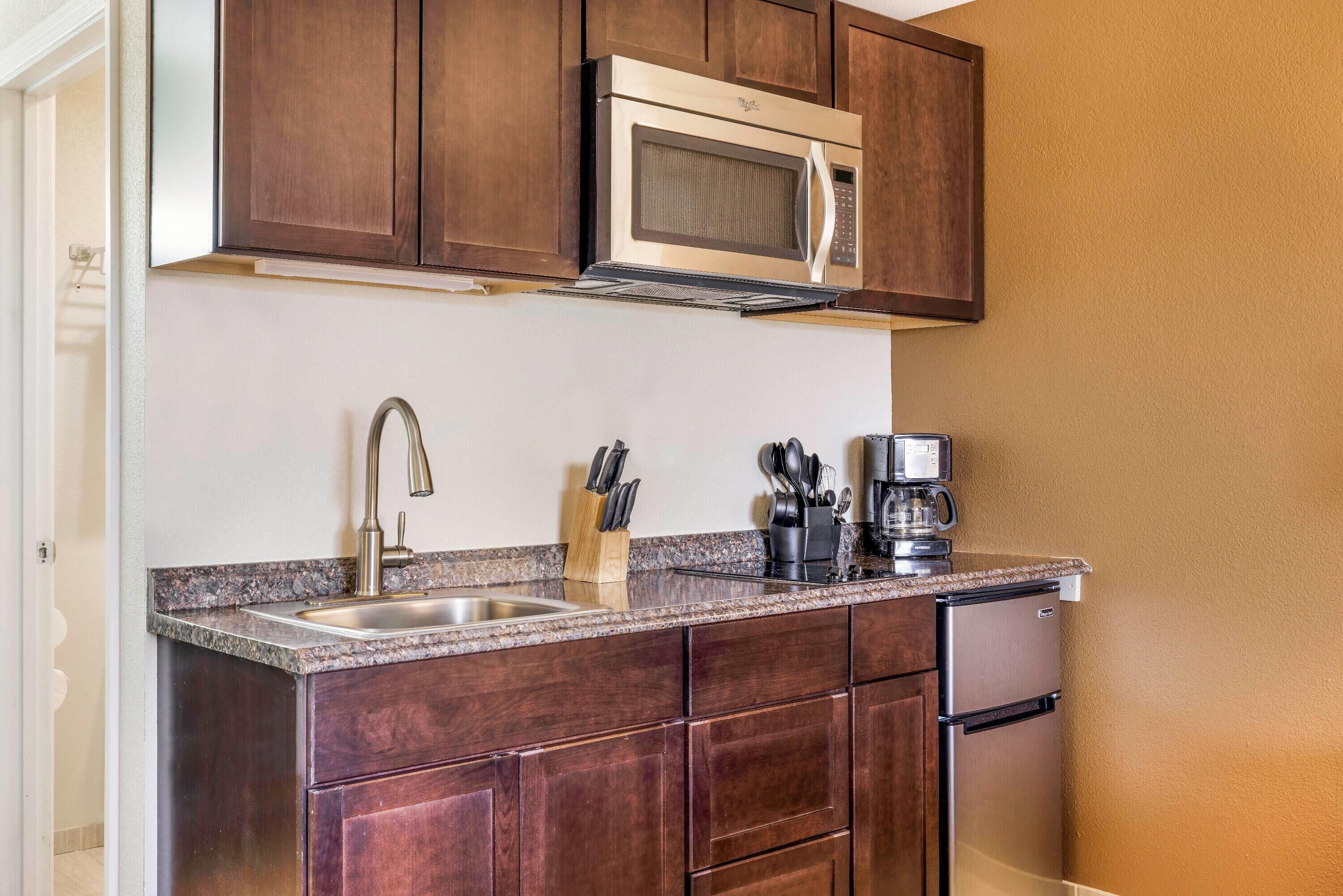 A compact kitchen with dark wooden cabinets, a stainless steel microwave, a coffee maker, and a sink with a modern faucet.