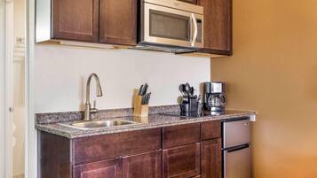 A compact kitchen with dark wooden cabinets, a stainless steel microwave, a coffee maker, and a sink with a modern faucet.