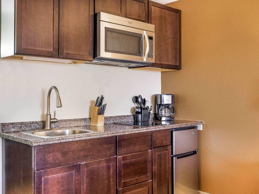 A compact kitchen with dark wooden cabinets, a stainless steel microwave, a coffee maker, and a sink with a modern faucet.