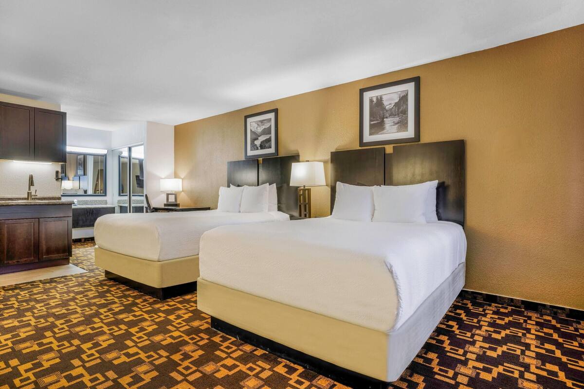 A hotel room with two beds, a desk, and a mirror.
