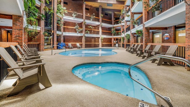 An indoor swimming pool with multiple levels of balconies, surrounded by lounge chairs and potted plants.