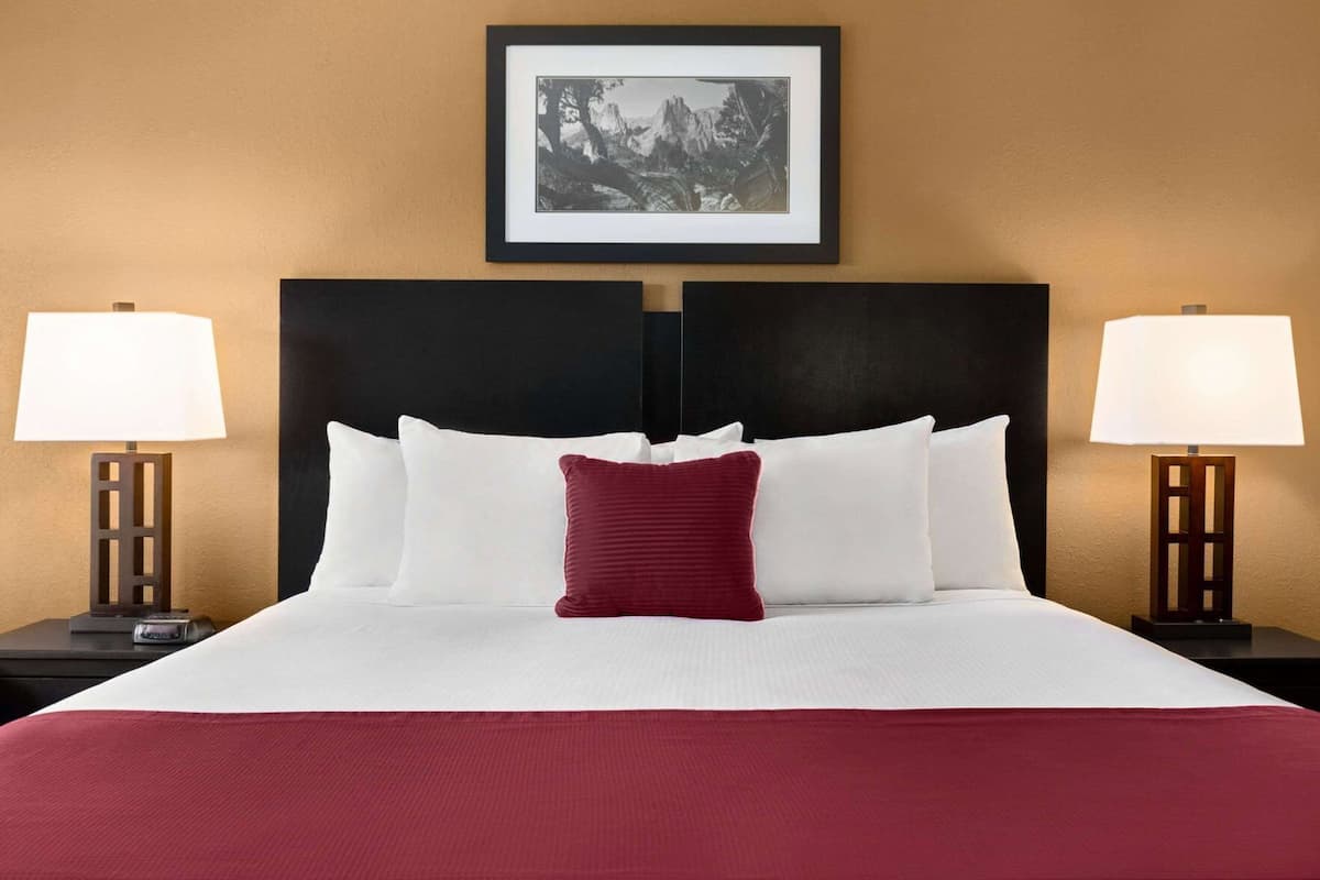 A neatly made bed with white and red pillows, a black headboard, and a framed picture above.